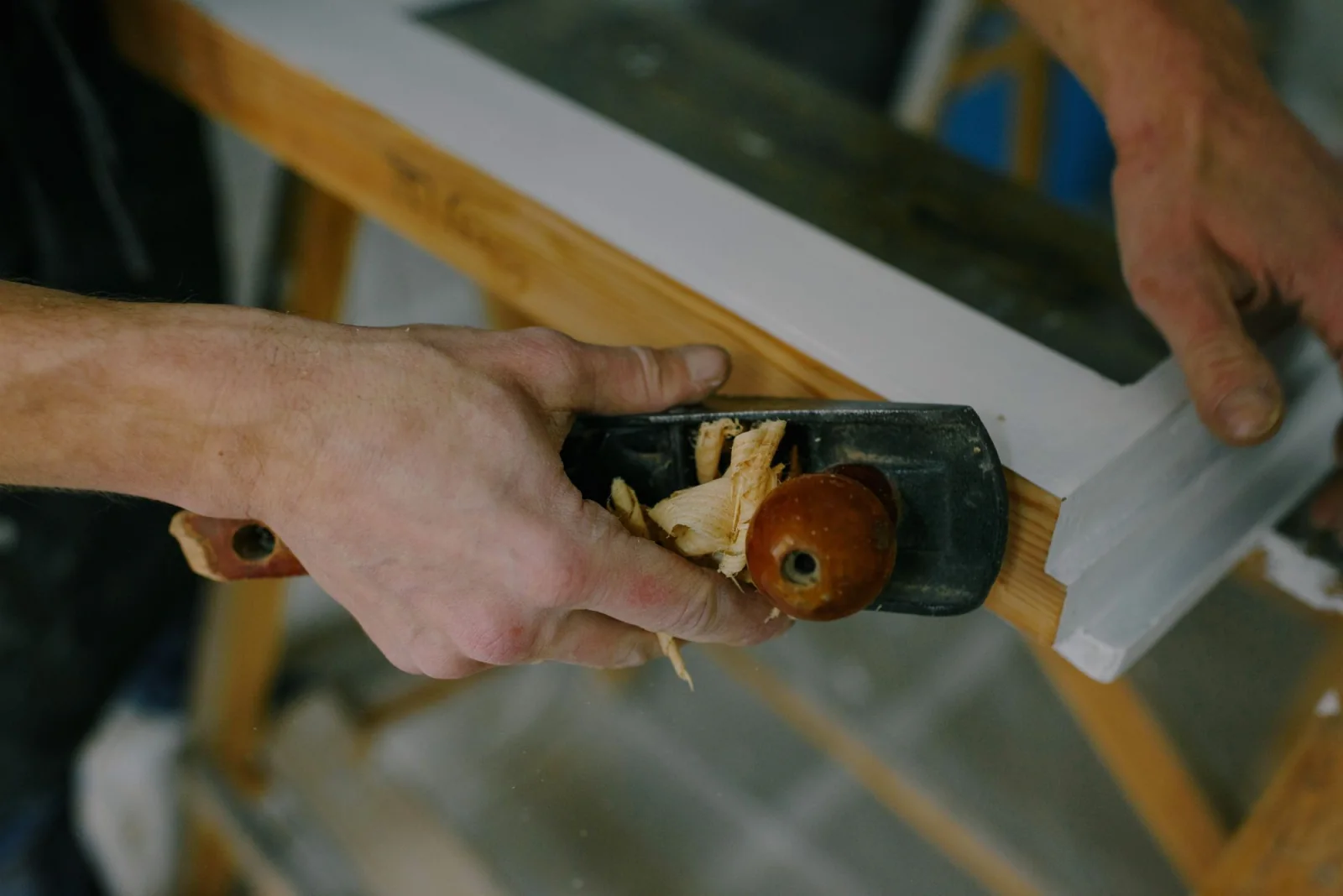 Hands using a hand plane on a wooden frame.