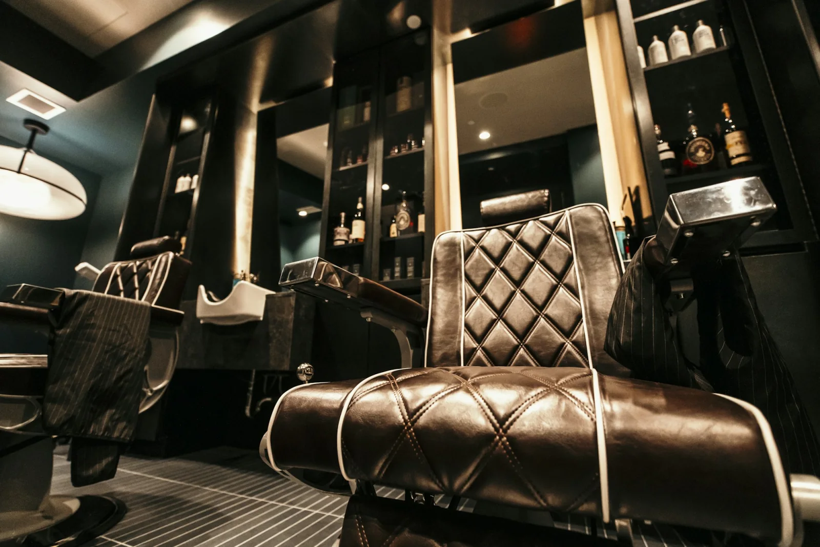Quilted leather barber chairs in front of mirrors in a warmly lit shop.