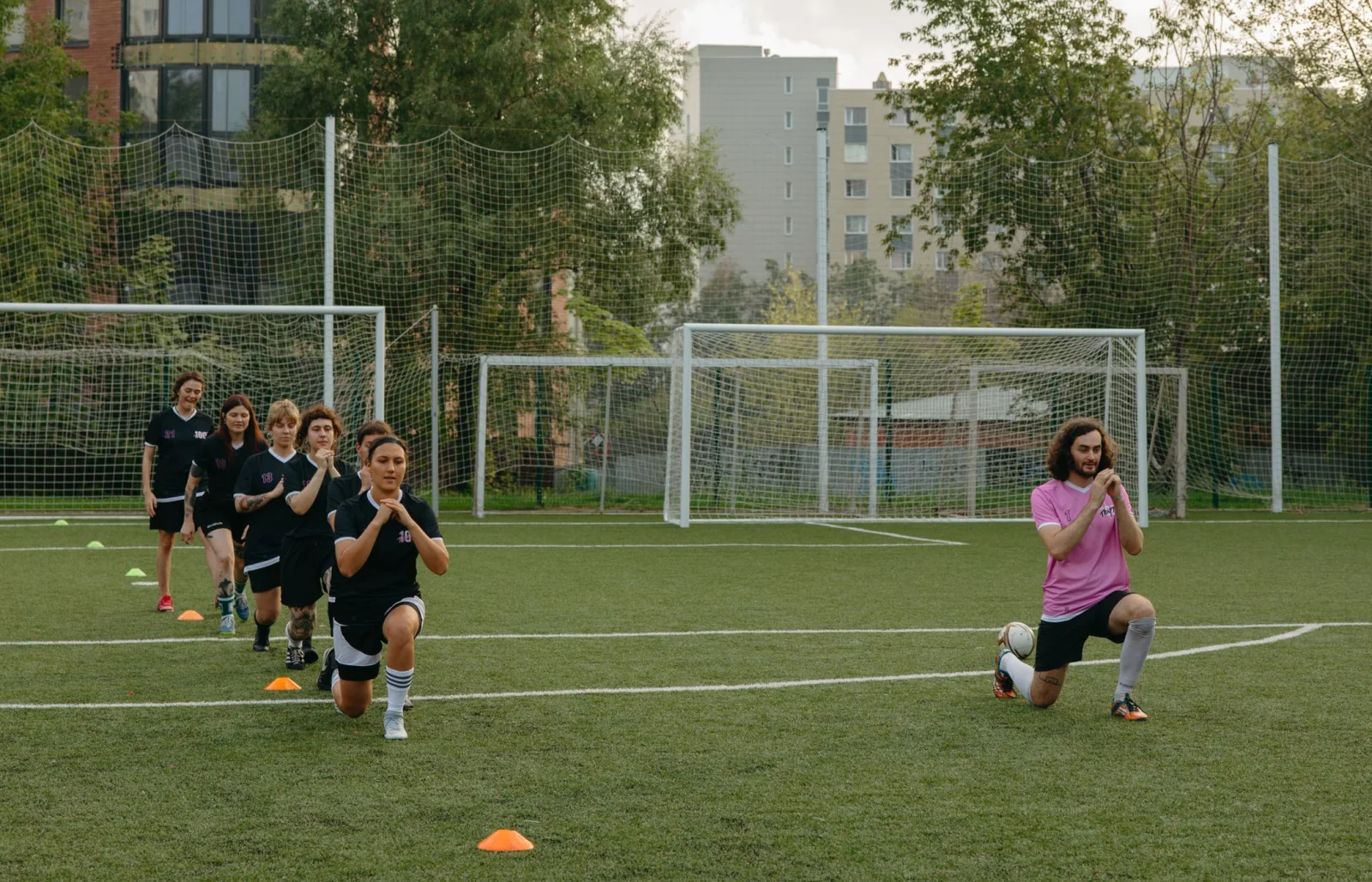 Young football players warming up with their coach on a grass pitch.